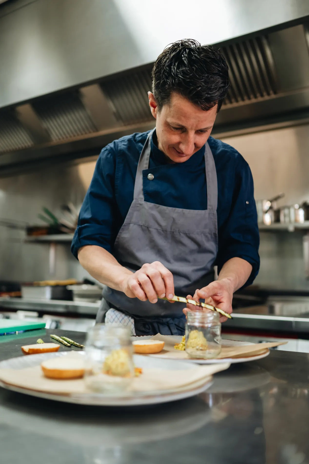 Een chef-kok in een professionele roestvrijstalen keuken die met zorg gegrilde asperges legt op een bord voor de lunch.